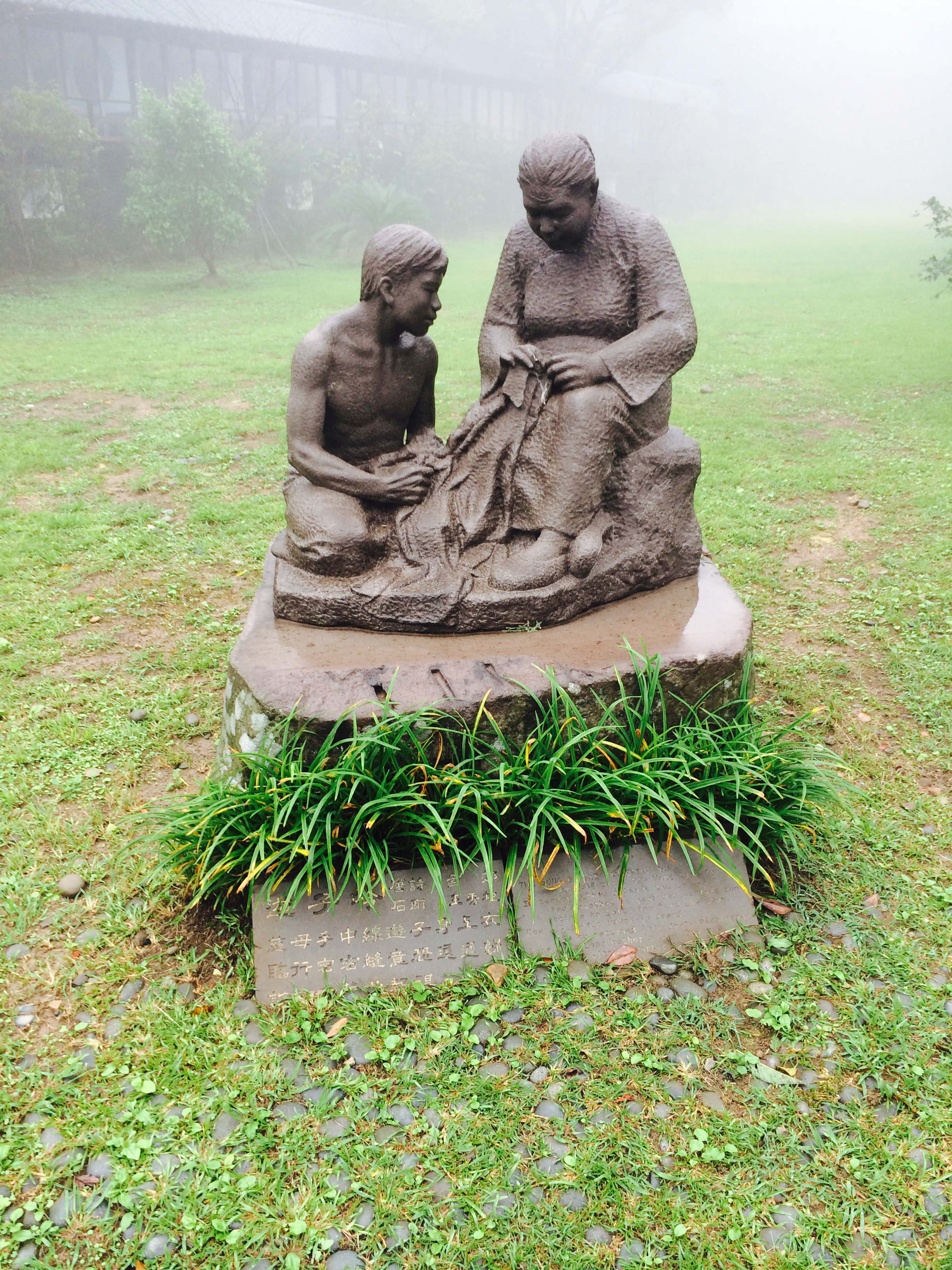 A statue of an older woman weaving or fixing cloth and a young man looks at her work